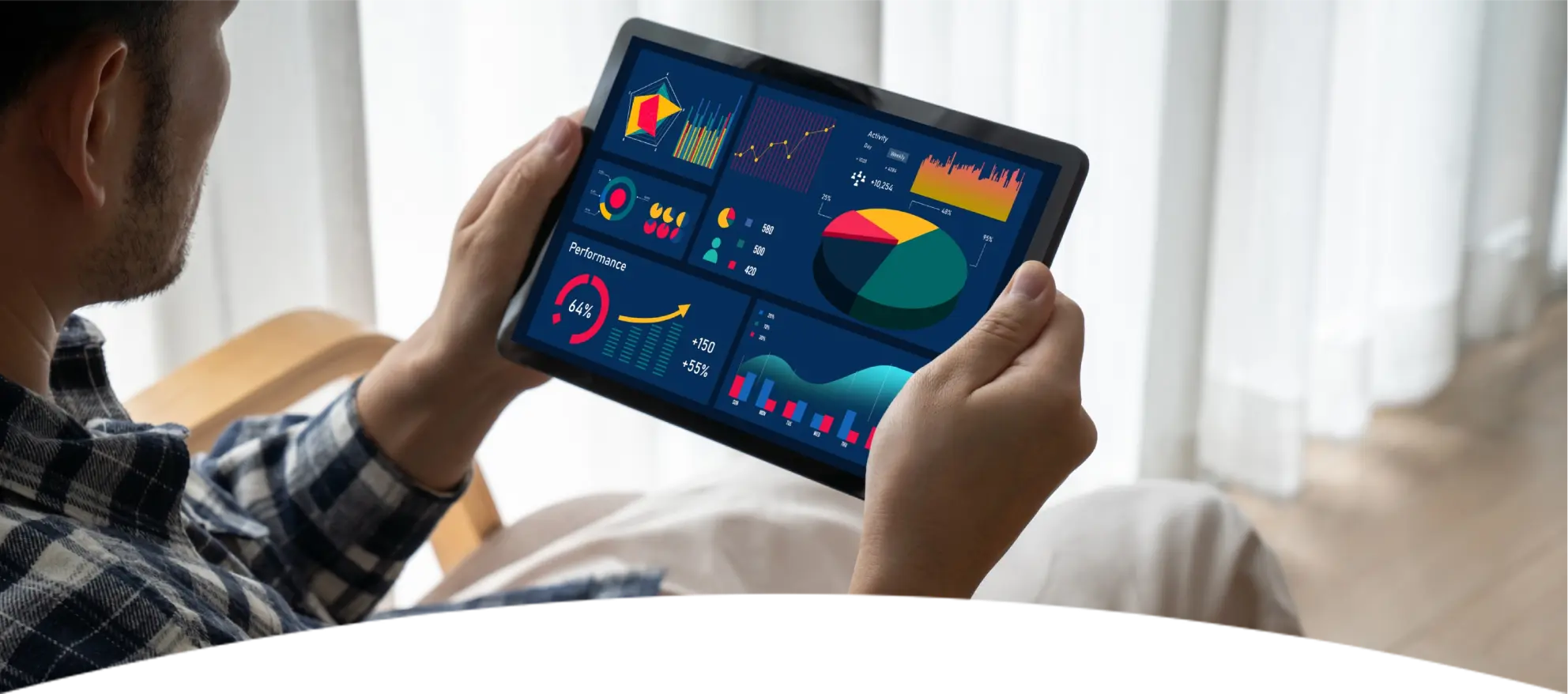 Een man in een geruit overhemd zit in een stoel met een tablet in zijn handen waarop kleurrijke grafieken en diagrammen te zien zijn, wat een beeld van concentratie en analyse oproept.